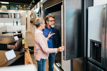 Middle aged couple, satisfied customers choosing fridge in appliances store.