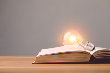 Clear light bulb with light effect on old book and put on wooden desk with grey space wall...