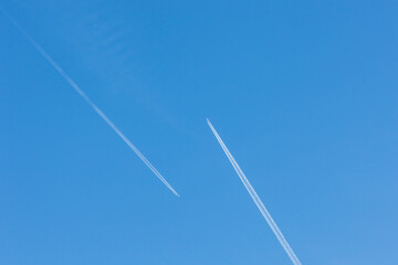 Two planes with white contrail meet head-on in blue sky