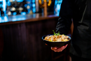 Men's waiter hands hold a Caesar salad with croutons, cheese, eggs, tomatoes and grilled chicken in pub