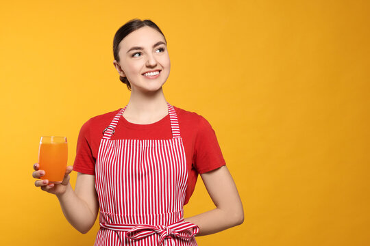 Beautiful young woman in clean striped apron with glass of juice on orange background. Space for text - Powered by Adobe