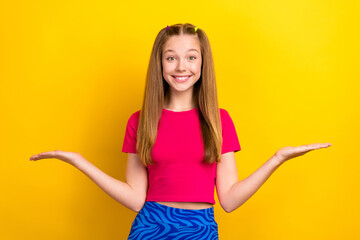 Portrait of optimistic lovely nice girl with long hairdo dressed pink top palms comparing products isolated on yellow color background