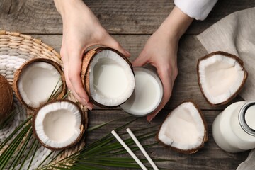 Woman holding tasty coconut near glass with milk at wooden table, top view