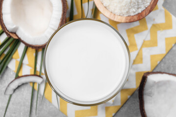 Glass of delicious coconut milk, flakes and coconuts on light grey table, flat lay