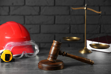 Construction and land law concepts. Gavel, scales of justice, hard hat, protective goggles and measuring tape on gray table against brick wall
