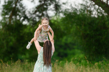 Portraits of a joyful mother and daughter spend time together, smile, have fun, enjoy happy family time and lift her up in the air in the park. Motherhood, lifestyle. Mothers Day