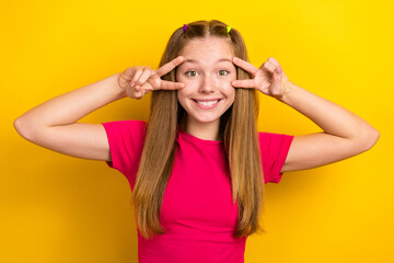 Obraz na płótnie Canvas Portrait photo of young smiling cheerful teenager girl wearing pink t-shirt face v-sign peace symbols blogger isolated on yellow color background