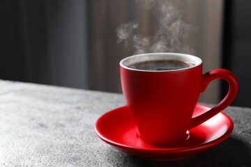 Red cup with hot steaming coffee on grey table indoors, space for text