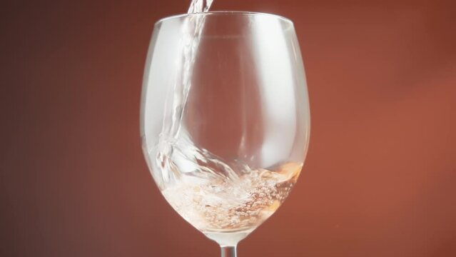 Close up of of rose wine being poured into a glass creating bubbles. Slow motion. 