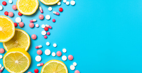 Medicine and health concept. Avitaminosis, pharmaceuticals. Vitamin C. Pink and white tablets, pills, capsules, vitamins with juicy lemon slices on blue background, flat lay top view copy space