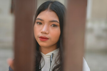 A pretty filipino woman as seen behind the fence of a gated house.