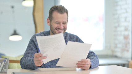 Middle Aged Man Celebrating Success while Reading Documents in Office