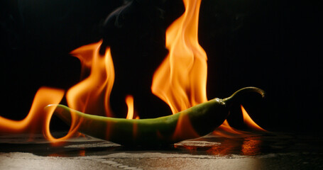 Hot green pepper set on flames. Epic cinematic shot of chili pepper burning in fire - art food concept close up photo 