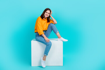 Full length photo of charming dreamy lady wear orange shirt sitting cube isolated turquoise color background