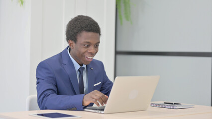 African Businessman Celebrating Online Success on Laptop in Office