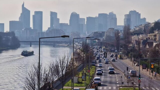 Busy traffic on highway and city streets creating high pollution and smog. Urban view across Seine river to La Defense metropolitan district, Paris, France