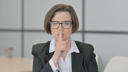 Old Businesswoman with Finger on Lips, Asking for Silence