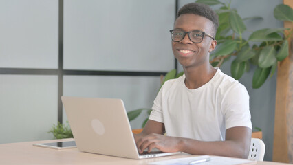 Young African Man Smiling at Camera while using Laptop