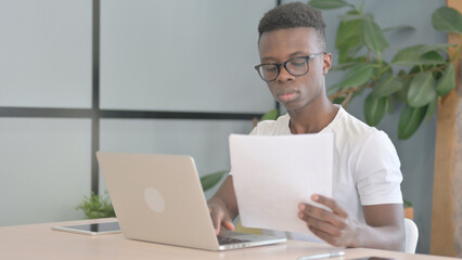 Fototapeta premium Young African Man Working on Documents and Laptop