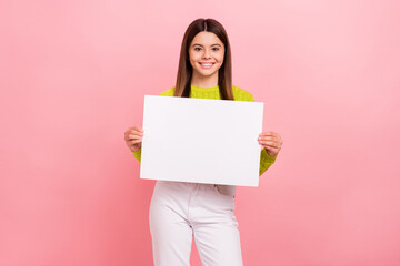 Photo portrait of lovely teen lady showing white paper sheet empty space dressed stylish green clothes isolated on pink color background