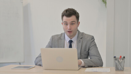 Young Businessman Celebrating Online Success on Laptop in Office