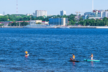 Active recreation on the board on the big river. Tourism on sap boards. Outdoor water sports. Surfers, standing on a board, ride the waves. SUP surfing training. View of the city embankment