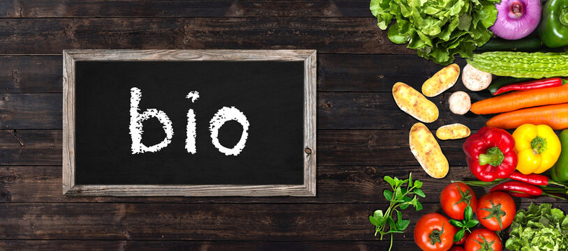 organic gardening concept - banner with vegetables and blackboard on brown wooden table