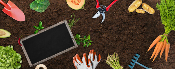 organic gardening concept - banner with vegetables, gardening tools and blackboard on brown soil