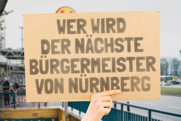 The phrase " Who's the next mayor of Nuremberg? " on a banner in men's hands blurred the background. Election. City management. Politics. Urban. Voter. Candidate