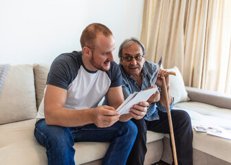 Grandad showing his son memories from past. A father sitting on a couch with his son and looking through a family album.