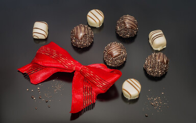 Chocolate pralines truffles decorated with red tied glittery bow. Confection, background designed...