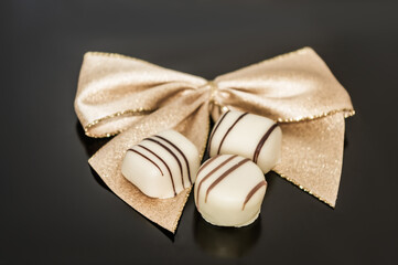 Gold ribbon tied into bow decorated with three piece of chocolate.