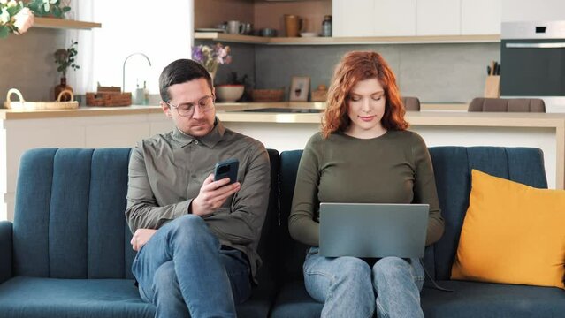 Modern Couple With Gadgets Sitting On The Sofa Do Not Communicate With Each Other. No Emotional, Dont Talking. Holding Smartphones And Looking At It. Couple Problems. Communication Problems.