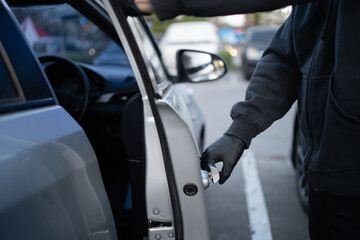 Close-up shot of a thief wearing a black shirt and black gloves. He tried to open the car door and tried to break in. car theft concept. - obrazy, fototapety, plakaty