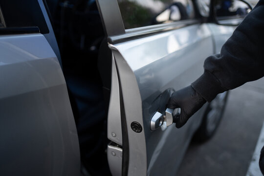 Close-up shot of a car thief hand pulling the handle of the car. Car theft concept.