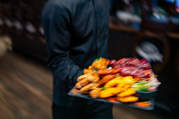 Waiter hold plate with set of assorted grilled meat platter with differend chicken and vegetables in restaurant. Motion blur