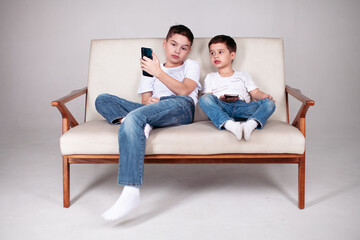 Obraz premium two brothers sitting on the sofa with phones
