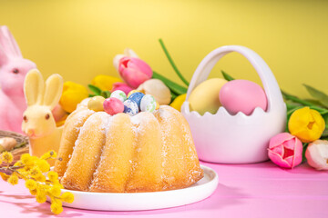 Traditional Easter round bundt cake. Sweet traditional Easter baking with sugar powder sprinkles, colorful Easter eggs, spring flowers, on pink yellow colorful background copy space