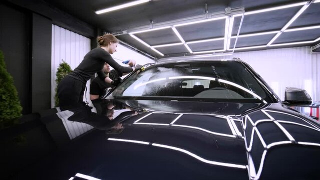 Professional car washer in black gloves wipes the car after washing and lining ceramics. Concepts of: Professional work, Various washing tools, Cleaning to shine.