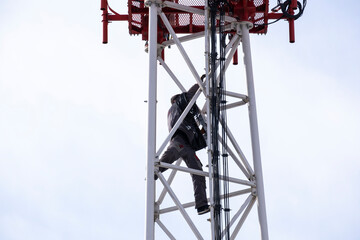 The fitter climbs to the top of the telecommunications tower with equipment, working at height. Communication tower service.