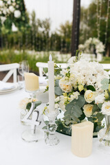 Composition for a festive wedding tables of white flowers of hydrangea, rose, eustoma and eucalyptus, different candles and a table number. Wedding outdoor concept