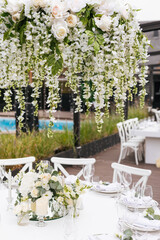 Served wedding table with decorative fresh white flowers and candles. Celebration details. Hanging flower beds and light bulbs Wedding decoration and decor, floristic concept