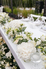 Wedding ceremony outdoor. Presidium for the newlyweds, decorated with candles and vases with white natural flowers such as eustoma, hydrangea, roses and eucalyptus