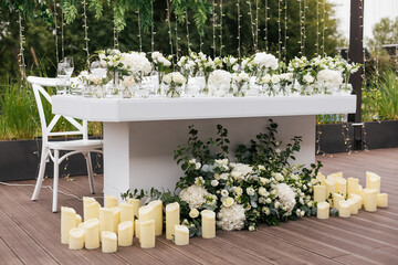 Wedding ceremony outdoor. Presidium for the newlyweds, decorated with candles and vases with white natural flowers such as eustoma, hydrangea, roses and eucalyptus