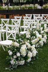 Wedding ceremony outdoor. White chairs decorated by fresh flower composition from white flowers, standing in the garden. Celebration day.