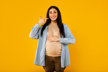 Beautiful woman expecting a baby, touching pregnant belly smiling and pointing with fingers at her perfect smile
