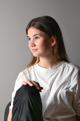 Portrait of a young beautiful teen model in jeans and white shirt on gray background. Vertical photo