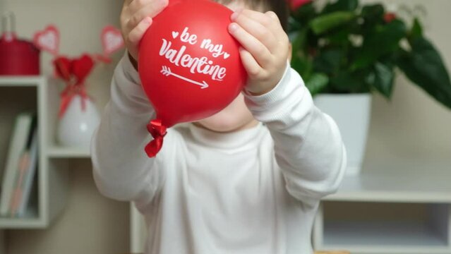 Cute 5 year old boy holds a balloon with the text be my valentine and smiles