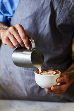 Crop barista pouring milk into cappuccino in cafe
