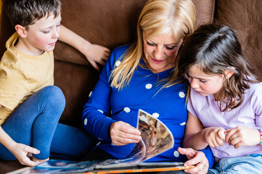 Focused mature woman and children looking at photo album book together